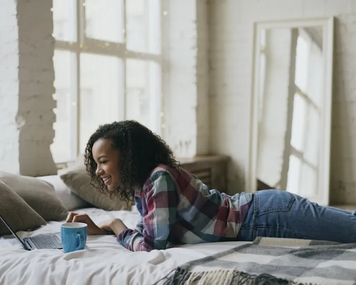Homeowner relaxing on a bed while checking her savings estimate on her phone